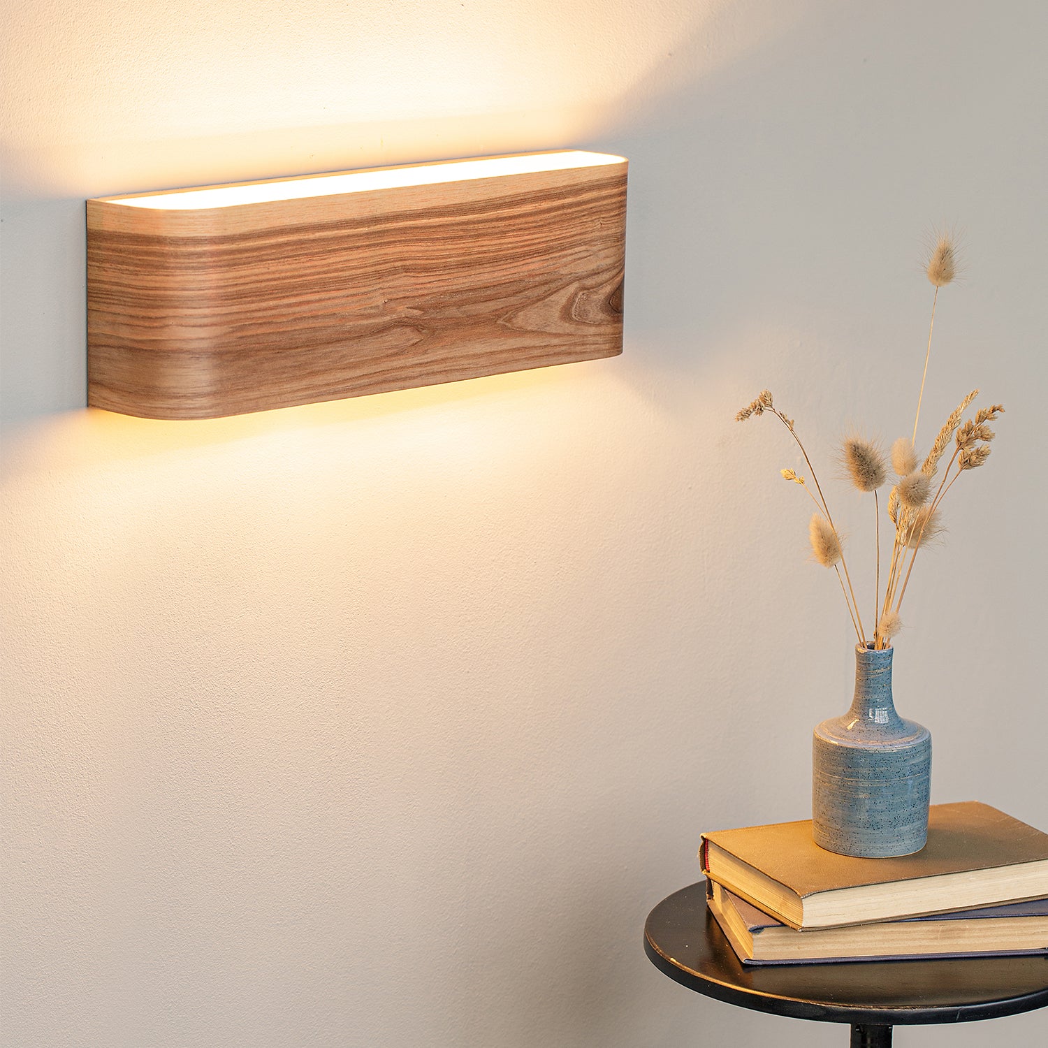 A lit ash veneer wall sconce glowing on a warm wall above a side table